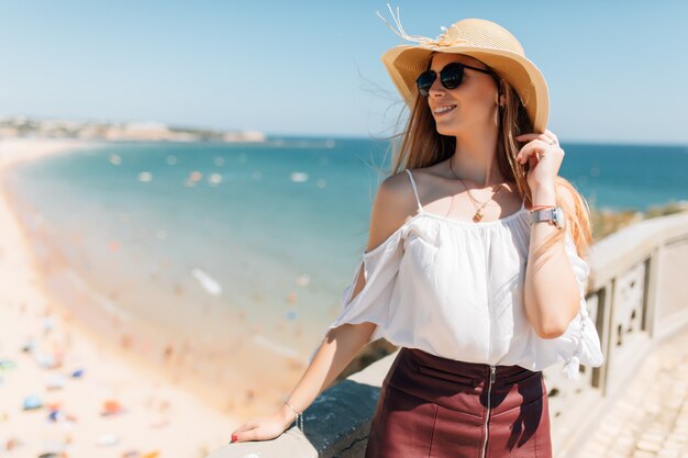 모자와 둥근 선글라스를 착용하는 젊은 여자의 초상화, 바다에 바람이 부는 날씨 좋은 여름날
