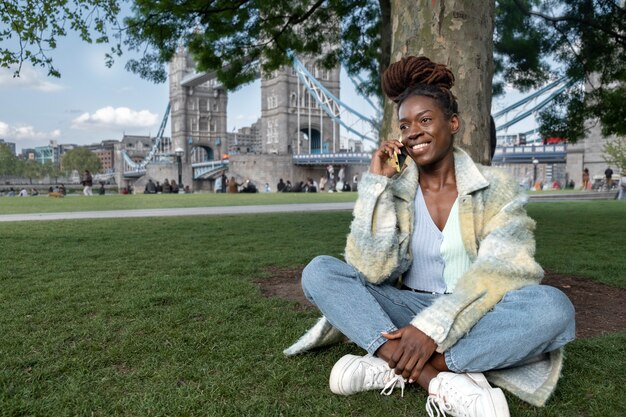 도시의 풀밭에 앉아 있는 동안 전화 통화를 하는 아프리카 향취를 가진 젊은 여성의 초상화