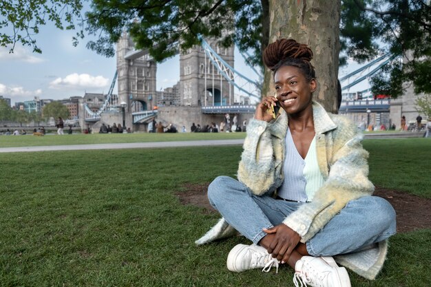 Portrait of young woman with afro dreadlocks talking on the phone while sitting on grass in the city