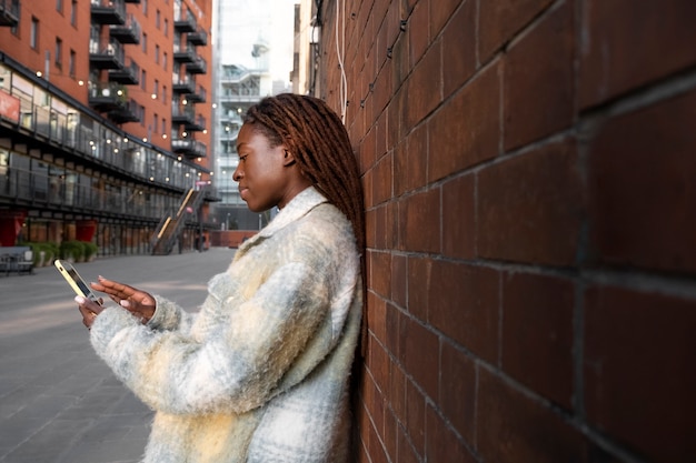 Foto gratuita ritratto di giovane donna con dreadlocks afro utilizzando smartphone all'aperto