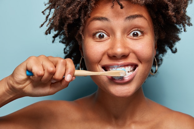 Portrait of young woman with afro haircut brushing her teeth