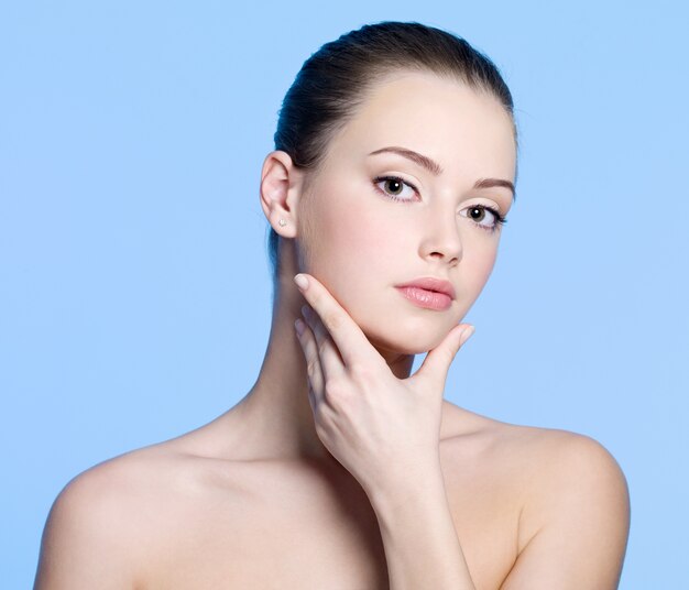 Portrait of young woman with beautiful clean fresh skin on face - blue background
