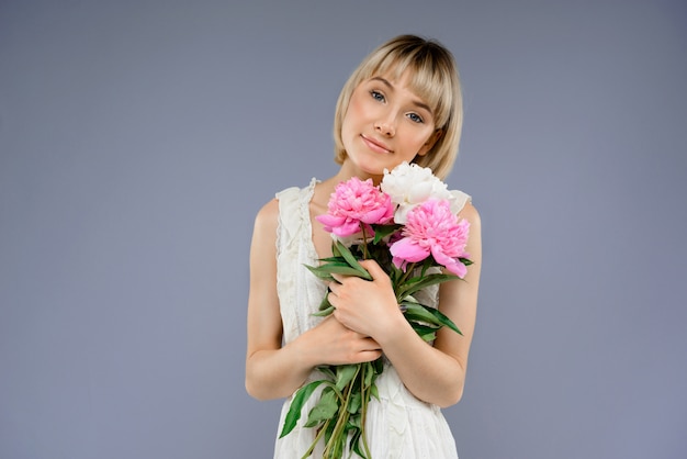 Portrait of young woman with bouquet flowers over grey backgro