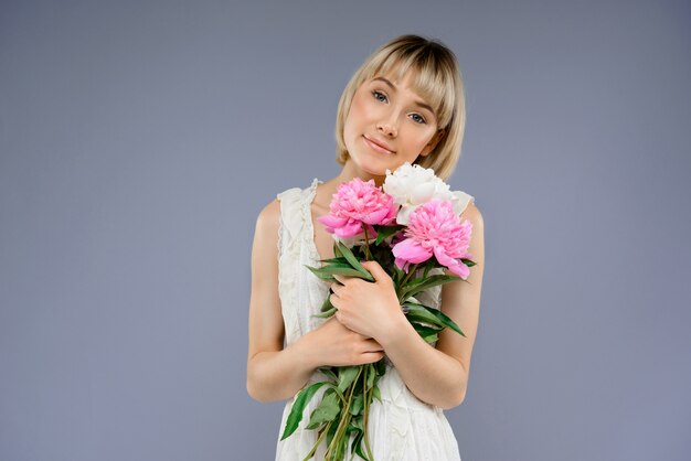 Portrait of young woman with bouquet flowers over grey backgro