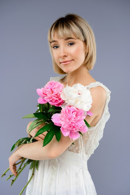 Portrait of young woman with bouquet flowers over grey backgro