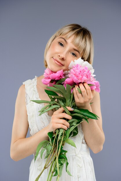 灰色のbackgroで花の花束を持つ肖像若い女性