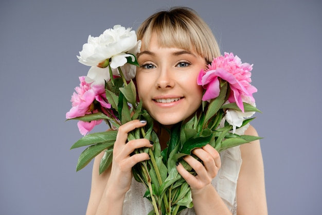Portrait of young woman with bouquet flowers over grey backgro