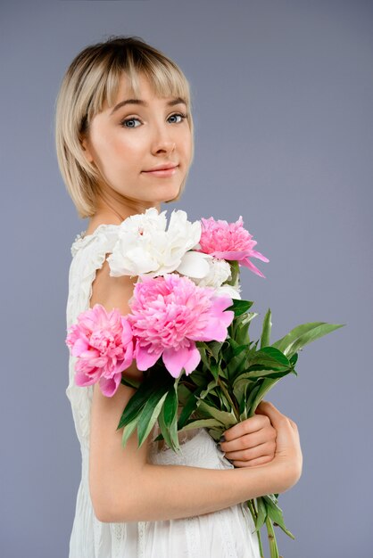 Portrait young woman with bouquet of flowers over grey backgro