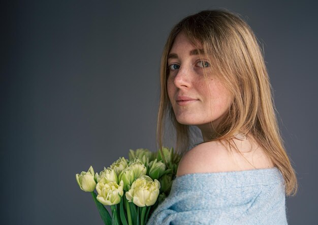 Portrait of a young woman with a bouquet of tulips on a gray background