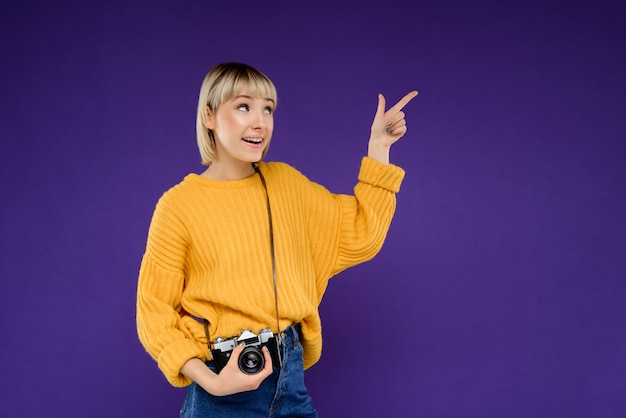 Portrait of young woman with camera over purple wall