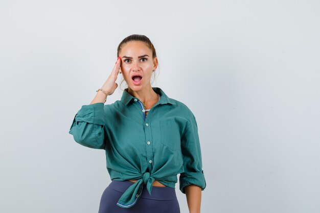 Portrait of young woman with hand on the side of face in green shirt and looking shocked front view