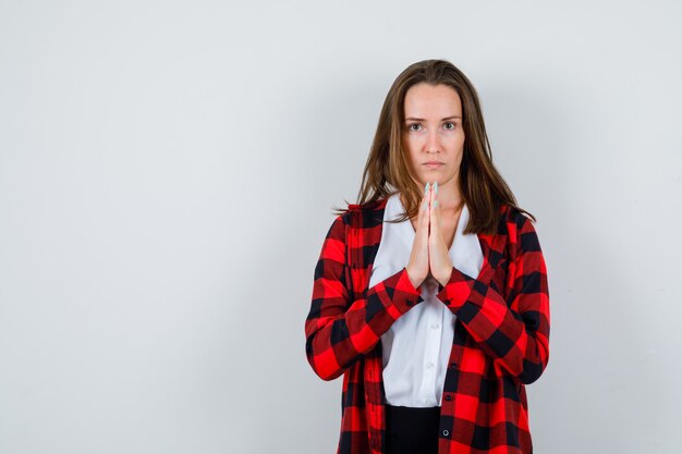 カジュアルな服装でジェスチャーを祈り、悲しい正面を見て手を持つ若い女性の肖像画