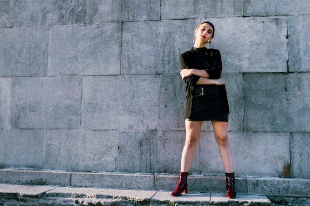 Portrait of a young woman with her arms crossed standing in front of wall