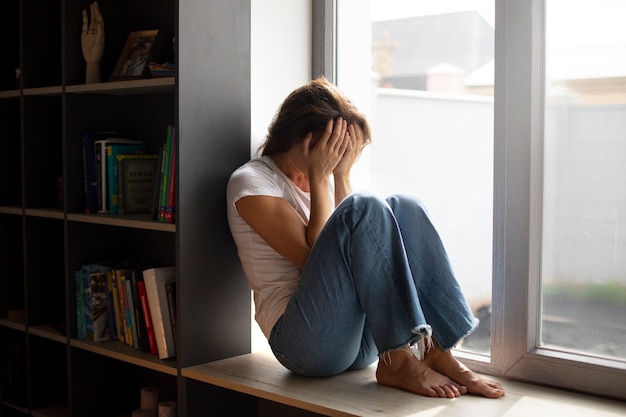 Free photo portrait of young woman with low self-esteem sitting by the window at home