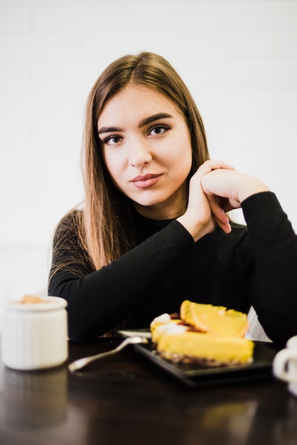 黒いテーブルの上のケーキのスライスを持つ若い女性の肖像画