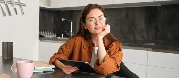 Free photo portrait of young woman working from home connecting to lesson on digital tablet reading in glasses