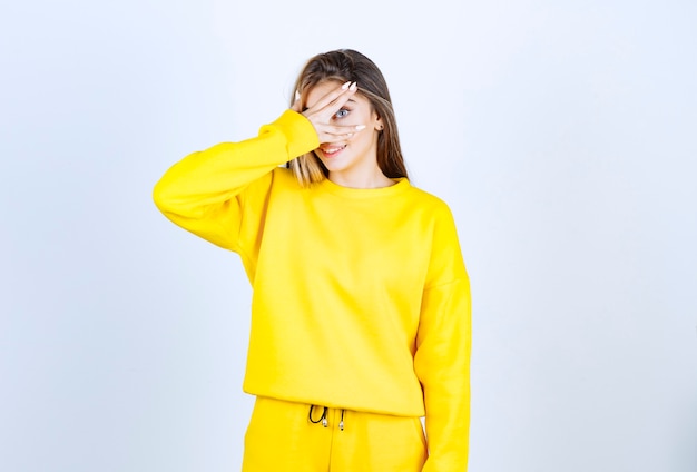 Portrait of young woman in yellow outfit standing and covering her eye