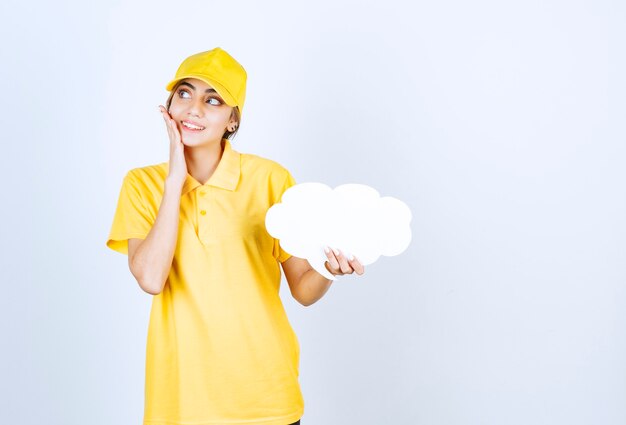 Portrait of a young woman in yellow uniform holding an empty white speech bubble cloud . 