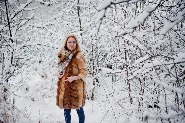 Portraiy of blonde girl in glasses red fur coat and scarf at winter day