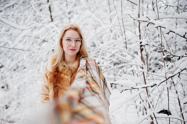 Portraiy of blonde girl in glasses red fur coat and scarf at winter day