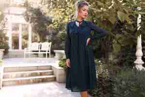 Free photo posing professional model in the back yard of the restaurant, wearing the green dress, hand on the waist, garden, outdoor, makeup, hair bun, red lips