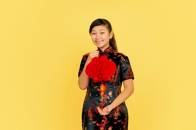 랜턴과 함께 포즈를 취하고 웃고 초대합니다. 해피 중국 설날. 노란색 바탕에 아시아 어린 소녀 초상화입니다. Copyspace.