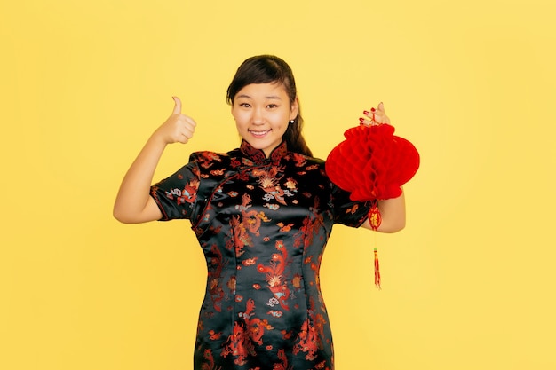 Posing with lantern, smiling, inviting. Happy Chinese New Year. Asian young girl portrait on yellow background. Copyspace.