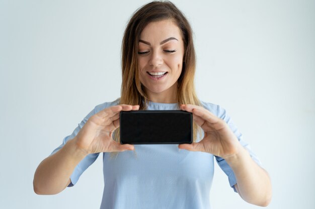 Positive adult woman showing smartphone screen. Lady advertising something. 