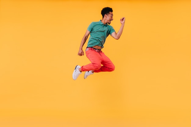 Positive african man in green t-shirt jumping. Indoor shot of blissful black guy expressing happy emotions.