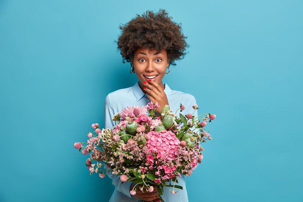 Positive Afro American woman holds beautiful bouquet of different flowers