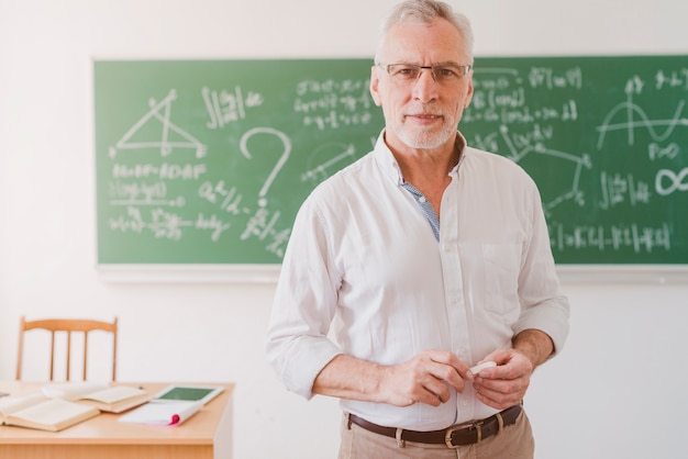 Positive aged math teacher standing with chalk