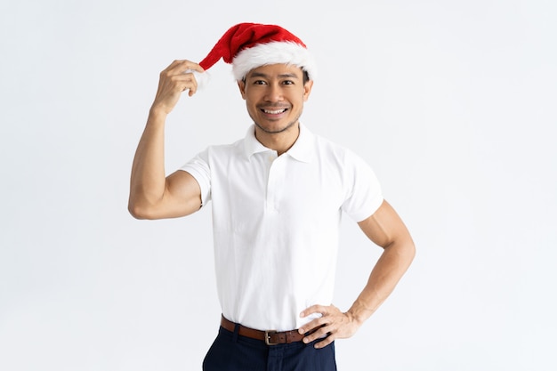 Положительный азиатский человек касаясь его шляпе Санта Клауса