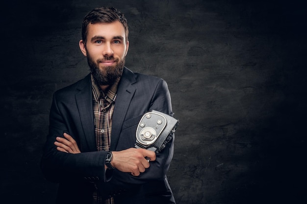 Free photo positive bearded cameraman holds vintage 8mm video camera in a studio on grey vignette background.