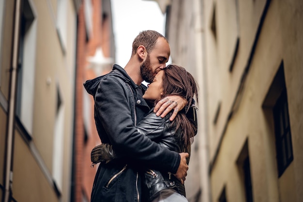 Positive bearded male kissing cute brunette female on a street in an old town.