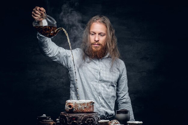 Positive bearded male pours hot water in a tea ceremony.