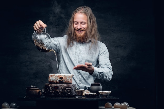 Free photo positive bearded male pours hot water in a tea ceremony.