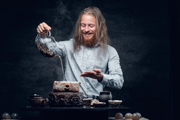 Positive bearded male pours hot water in a tea ceremony.