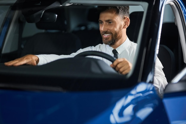 Positive bearded man examining car cabin at modern showroom