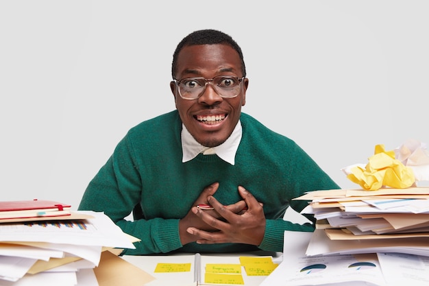 긍정적 인 흑인 남성 노동자는 서류 작업, 대학 시험 공부, 두 손을 가슴에 대고 진지하게 미소를 짓고, 안경을 통해 바라본다.