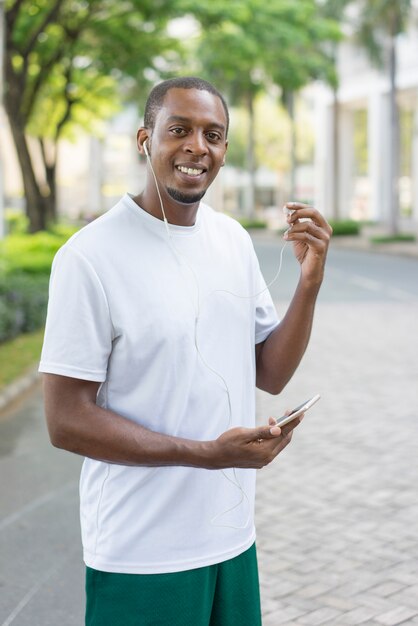 Positive black sportsman enjoying music with smartphone.