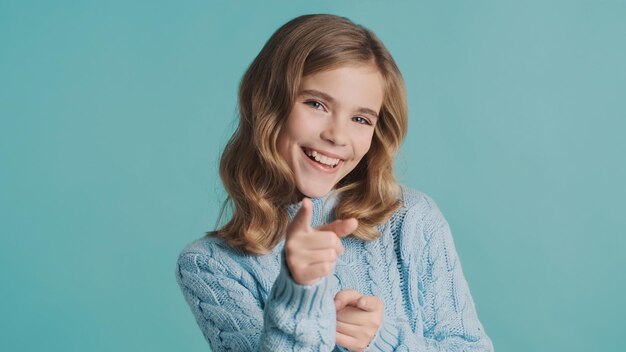 Positive blond teenage girl indicate straightly at camera with index fingers looking happy over blue background. Cool expression