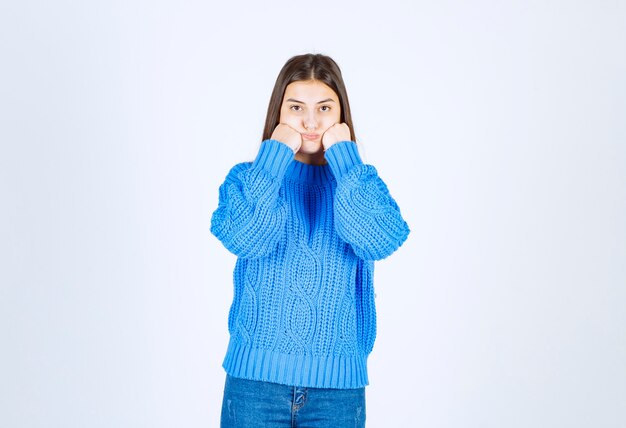 Positive brunette girl in blue sweater standing on white.