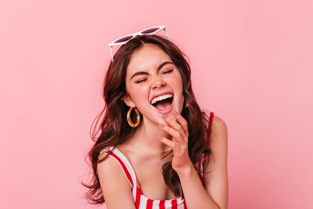 Positive brunette lady in golden massive earrings sincerely laughs on isolated wall