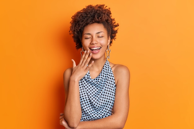 Positive carefree African American woman laughs happily keeps eyes closed