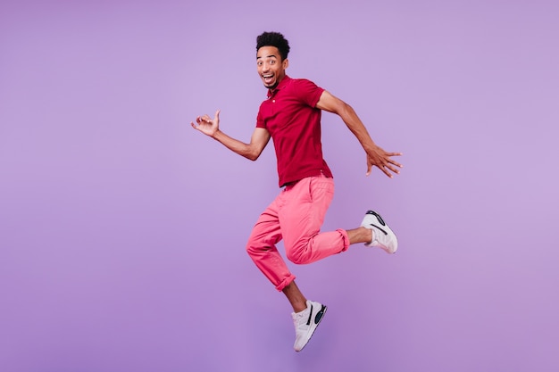 Uomo africano spensierato positivo in scarpe sportive ballando. bel ragazzo felice in pantaloni rosa che salta con il sorriso.