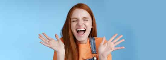 Foto gratuita positivo spensierato trionfante giovane attraente ragazza dai capelli rossi urla forte gioia felicità occhi chiusi