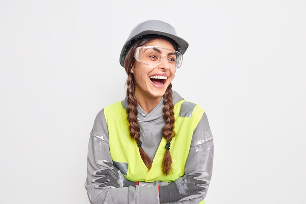 Foto gratuita l'ingegnere positivo e spensierato della donna ride felicemente tiene le braccia conserte distoglie lo sguardo soddisfatto del rapido lavoro di costruzione