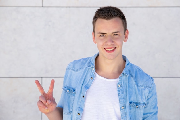 Free photo positive cheerful student guy making peace sign