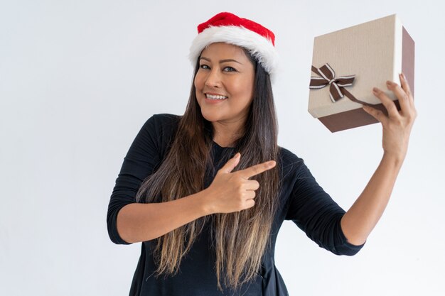 Positive Christmas lady showing gift at camera