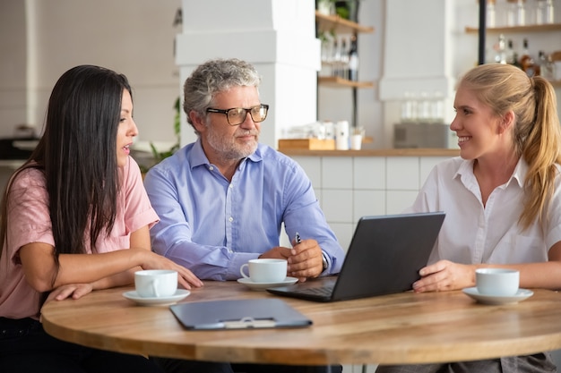 Positive confident agent showing project presentation on laptop to young and mature customers